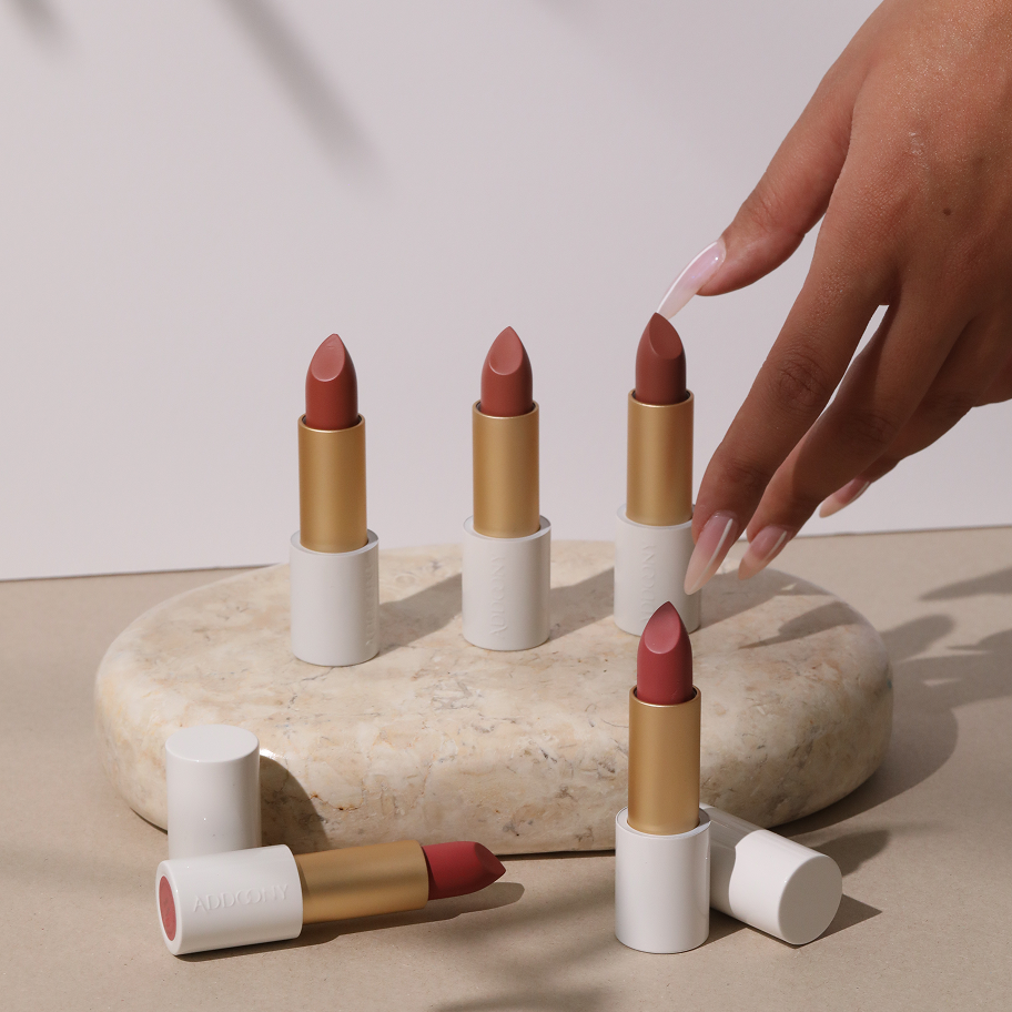 Set of lipsticks with a hand interacting with one on a stone surface