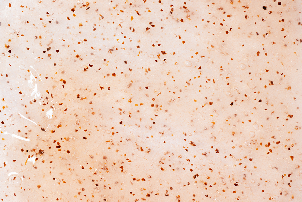 A close-up texture shot of a translucent, frosted glass or acrylic surface decorated with numerous small, scattered brown specks or flecks.
