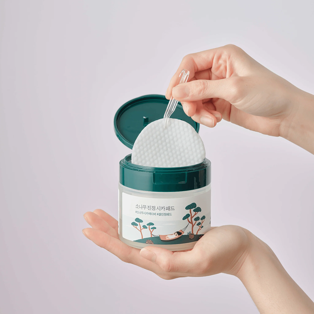 Hand holding a container with a white ball and a spoon, against a light gray background