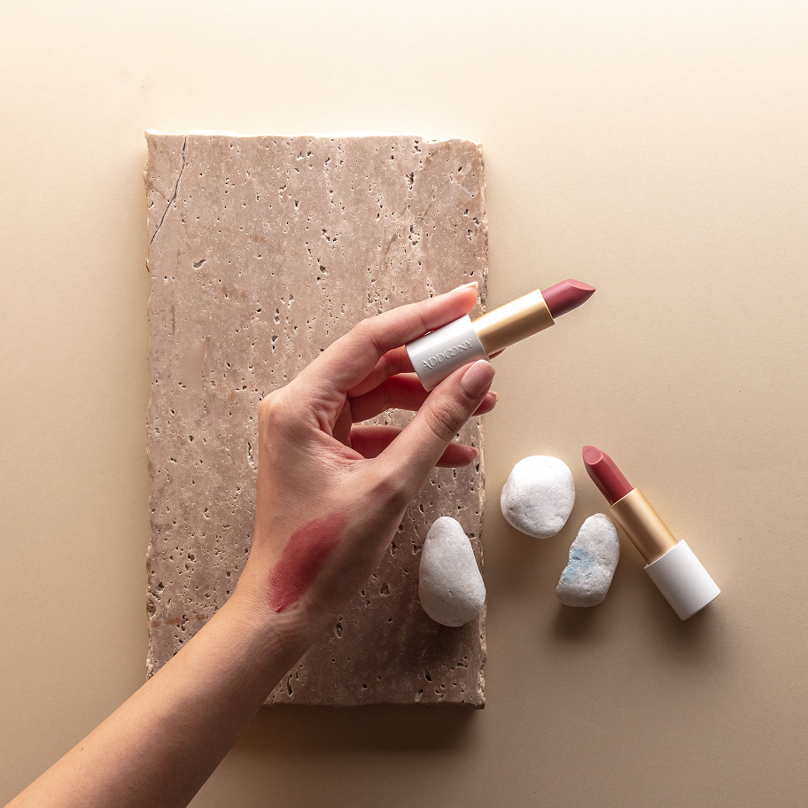 Hand holding a lipstick with swatch on beige background