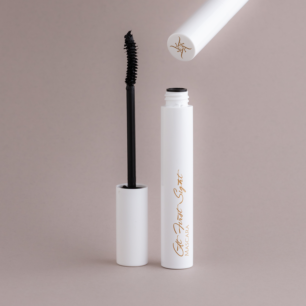 Mascara with open cap on a beige background