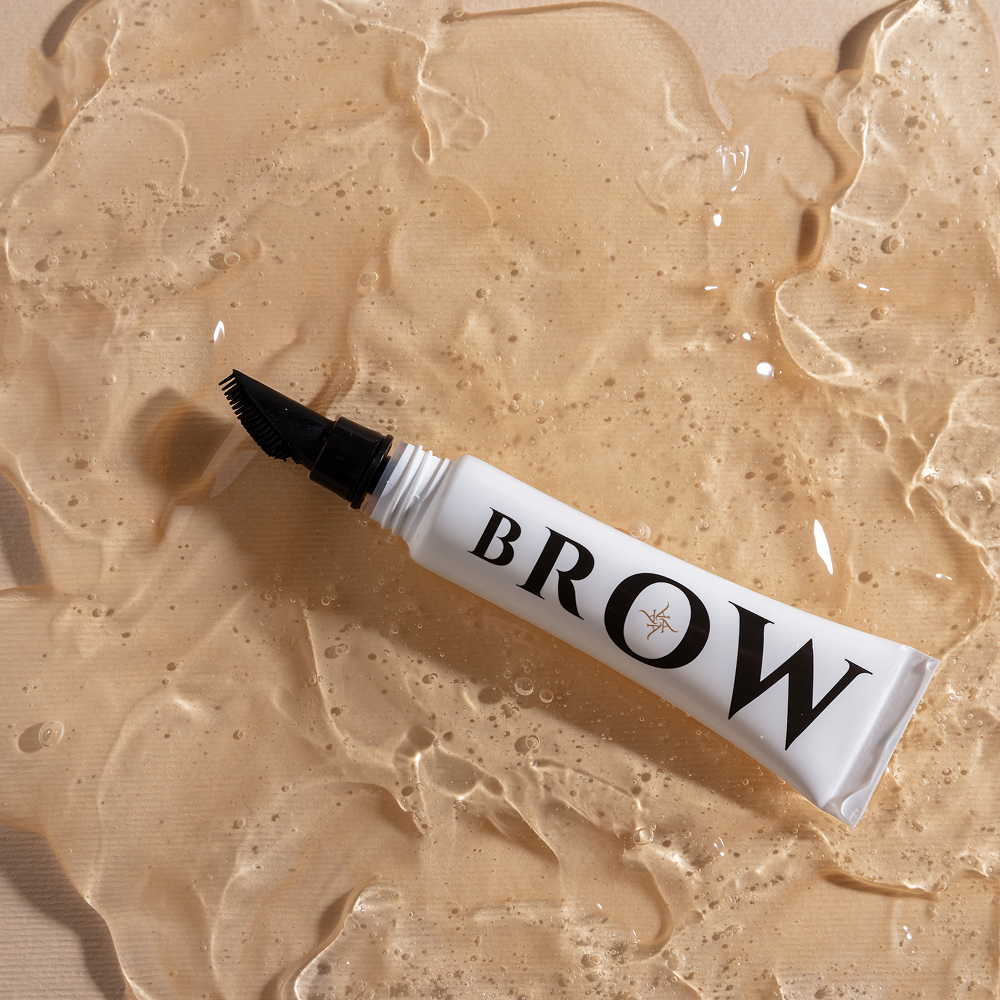 Tube of brow product on a beige textured background