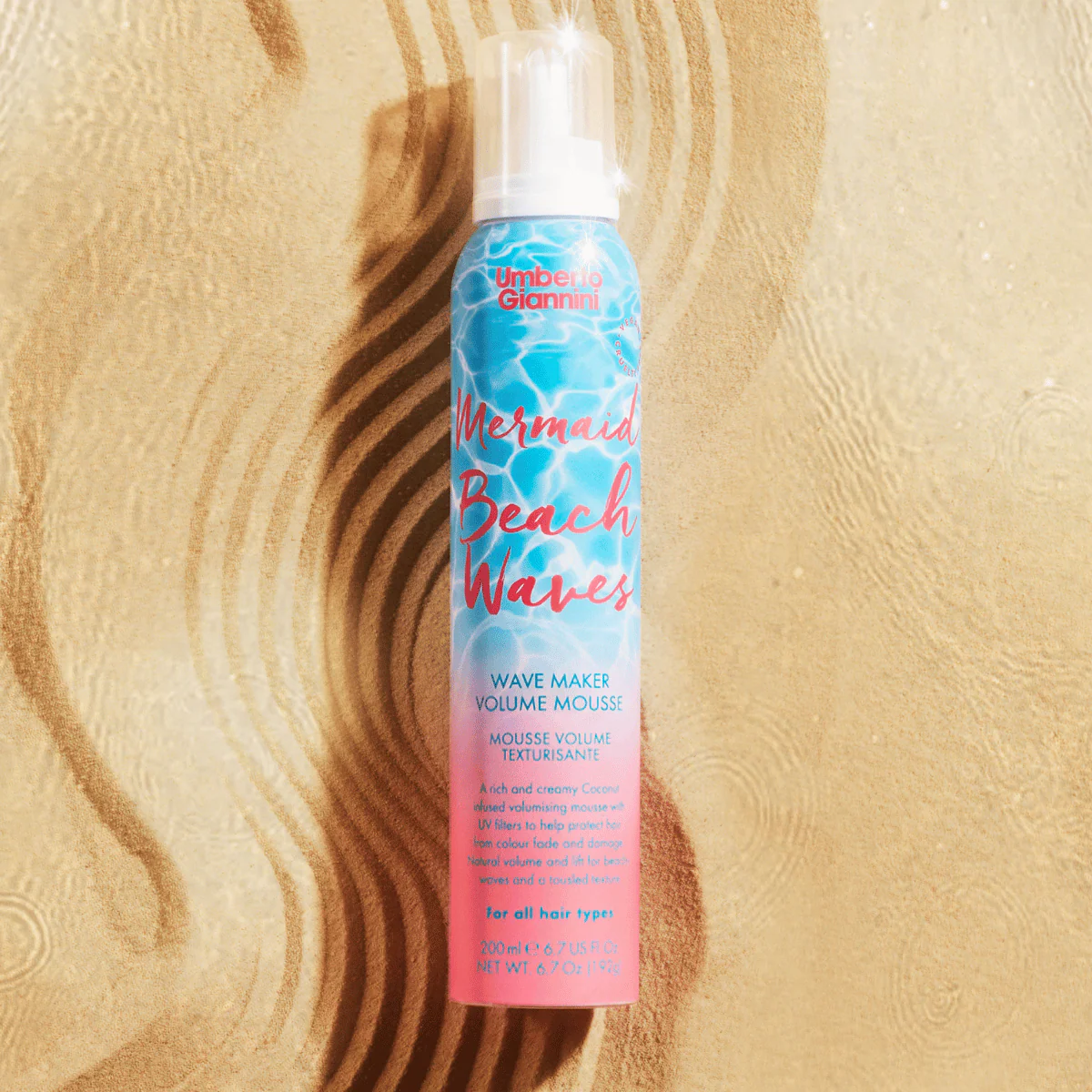 Hair mousse bottle labeled 'Mermaid Beach Waves' on a sandy background