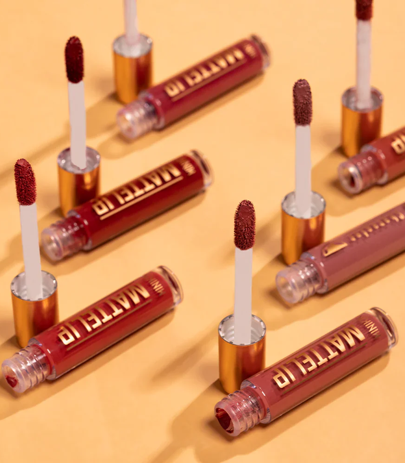 Multiple matte lip gloss tubes with applicators on a beige background