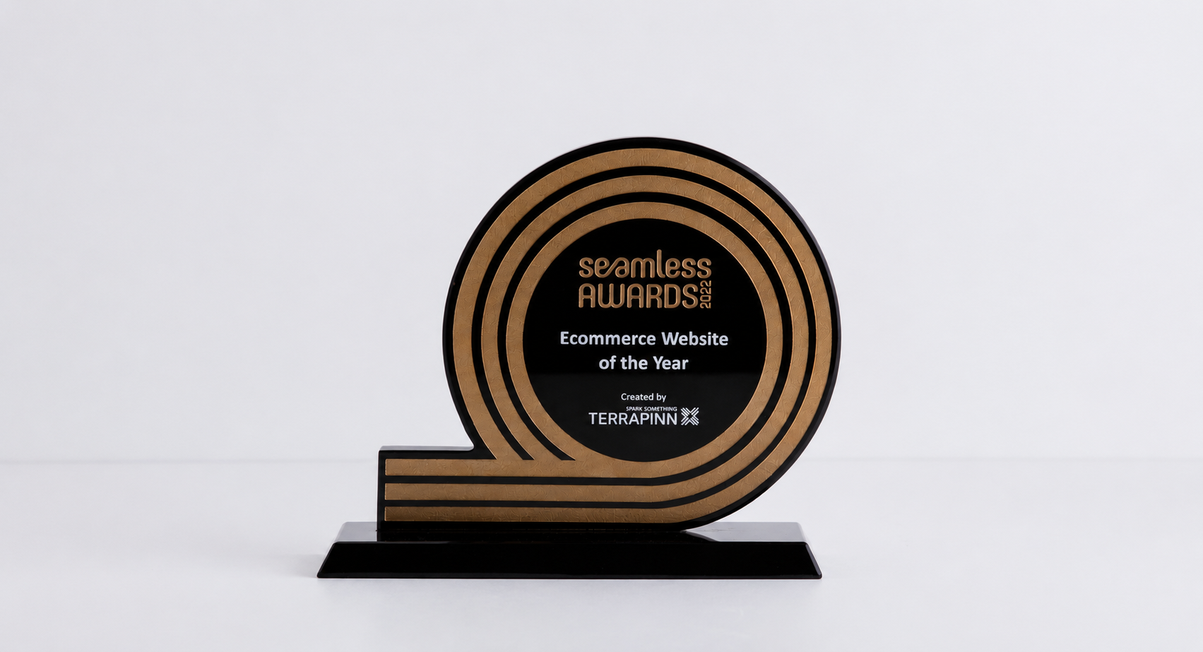 A circular black and gold award plaque on a black base, reading 'seamless AWARDS Ecommerce Website of the Year' with Terrapin branding, photographed against a clean white background.